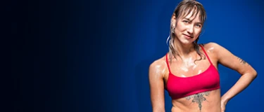 Junge Frau in rotem Sport-BH, nass von Wasser, vor einem blauen Hintergrund, mit Tätowierung.